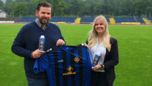 Nils Lappahn und Lisa Marie Zühlke halten TuS Koblenz Trikot und TuS-Wasser in der Hand, im Hintergrund Stadion Oberwerth.