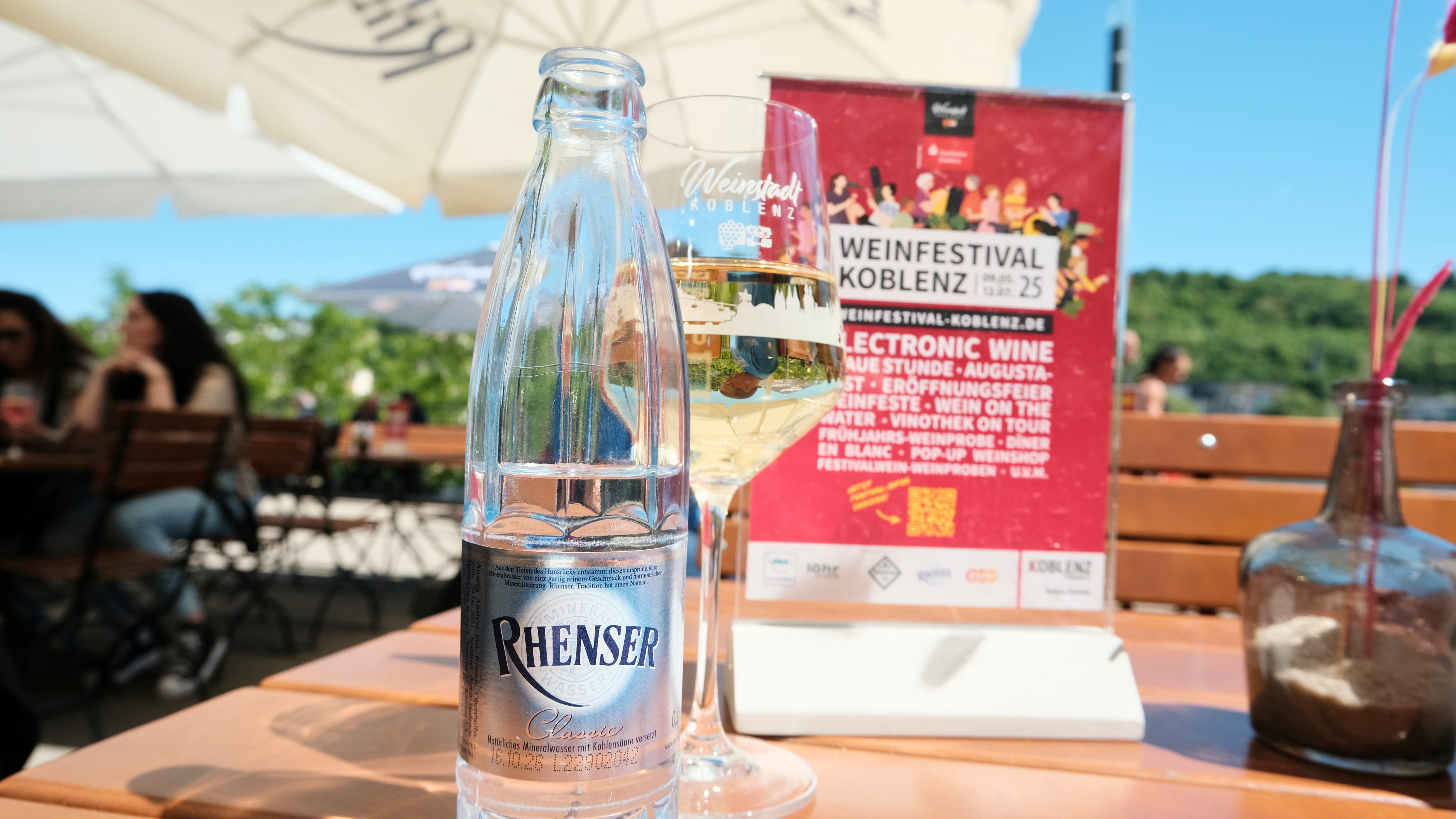 Rhenser Mineralwasser Glasflasche vor Weinglas und Aufsteller vom Weinfestival Koblenz.