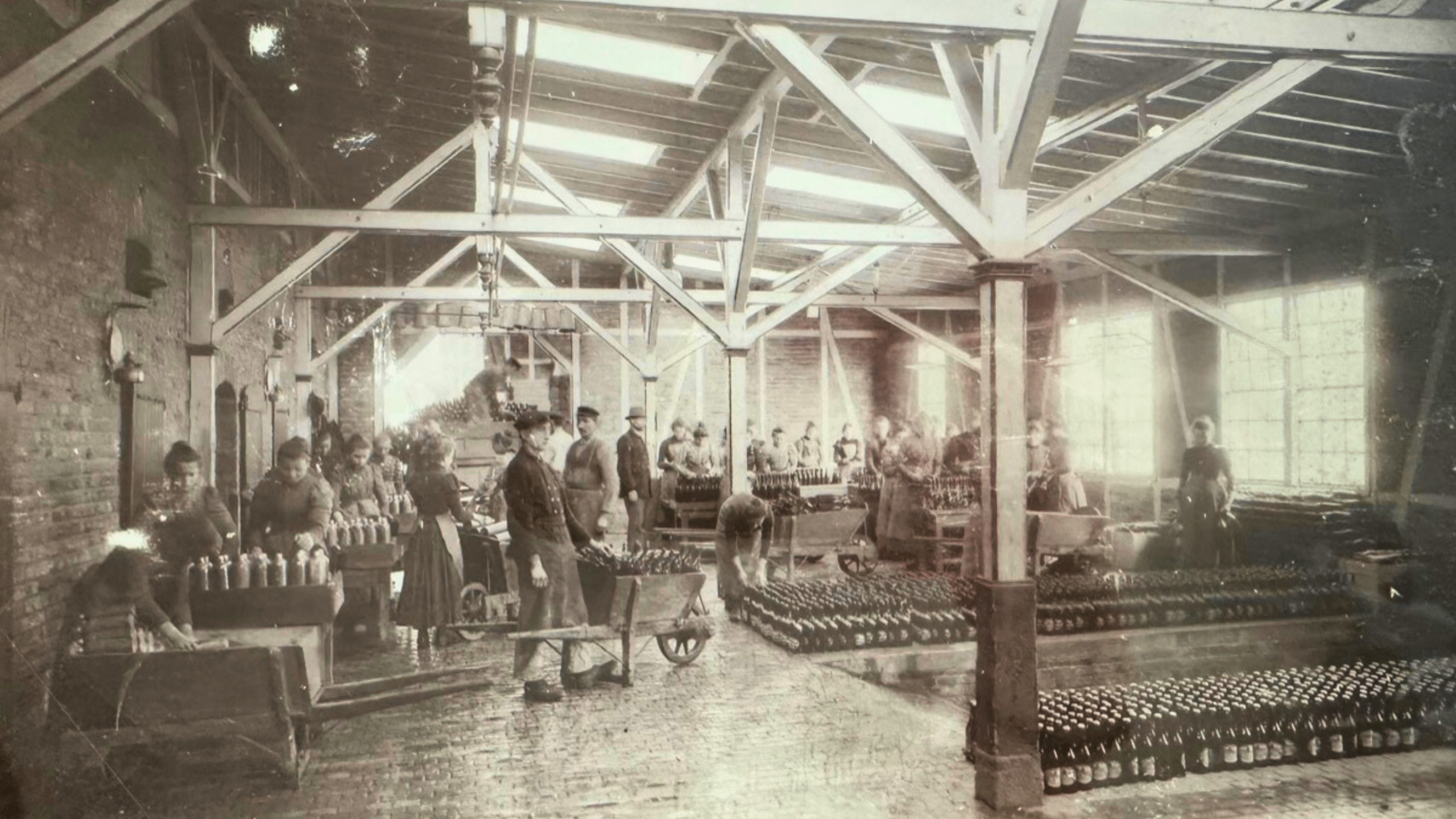 Schwarz-Weiß-Foto von Rhenser Abfüllhalle mit Männern und Frauen im Handbetrieb, die Flaschen sortieren und verpacken.
