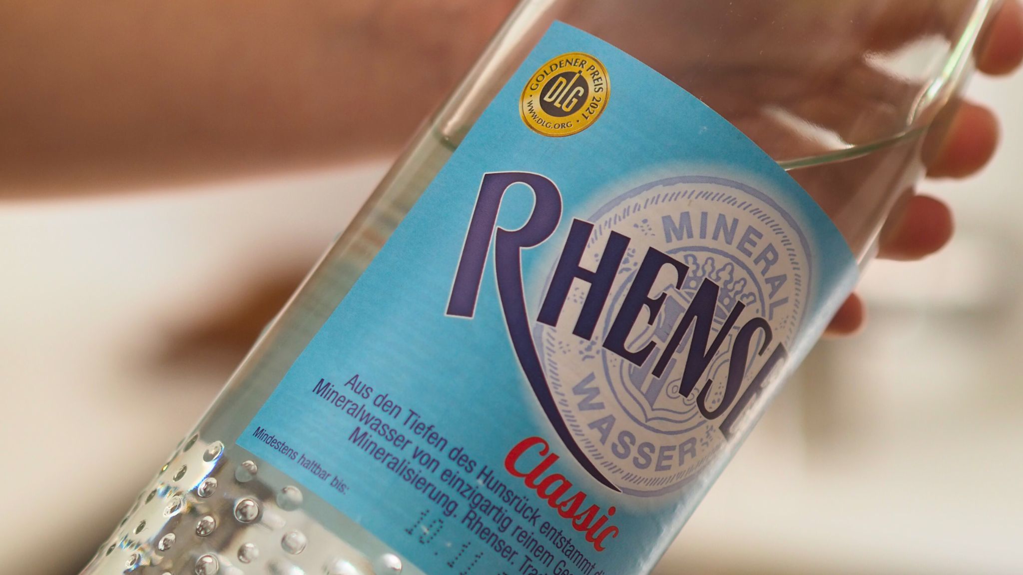 Hand hält eine Flasche Rhenser Mineralwasser Classic mit blauem Etikett.