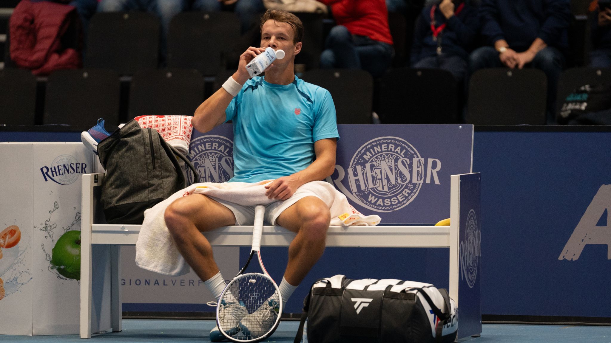 Tennisspieler sitzt während der Koblenz Tennis Open 2026 auf der Spielerbank und trinkt Rhenser Mineralwasser in der EPG Arena Koblenz.