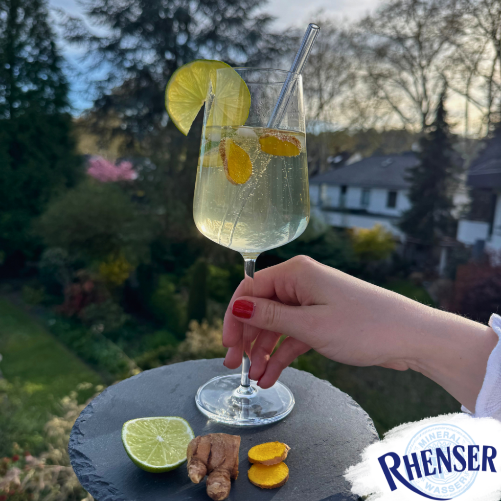 Ein Weinglas mit einem Citrus-Spritz Getränk. Serviert auf einer Schieferplatte mit frischen Limettenscheiben und Ingwerstücken.