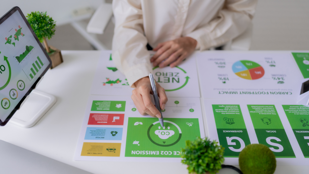Person analysiert Nachhaltigkeits- und CO₂-Infografiken an einem Schreibtisch mit Tablet und Pflanzen.
