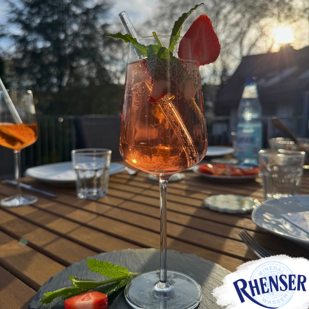Ein Weinglas mit einem Rosé-Spritz-Getränk. Serviert auf einer Schieferplatte mit frischen Erdbeerscheiben und Minzblättern.