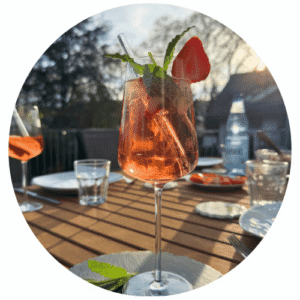 Ein Weinglas mit einem Rosé-Spritz-Getränk. Serviert auf einer Schieferplatte mit frischen Erdbeerscheiben und Minzblättern.