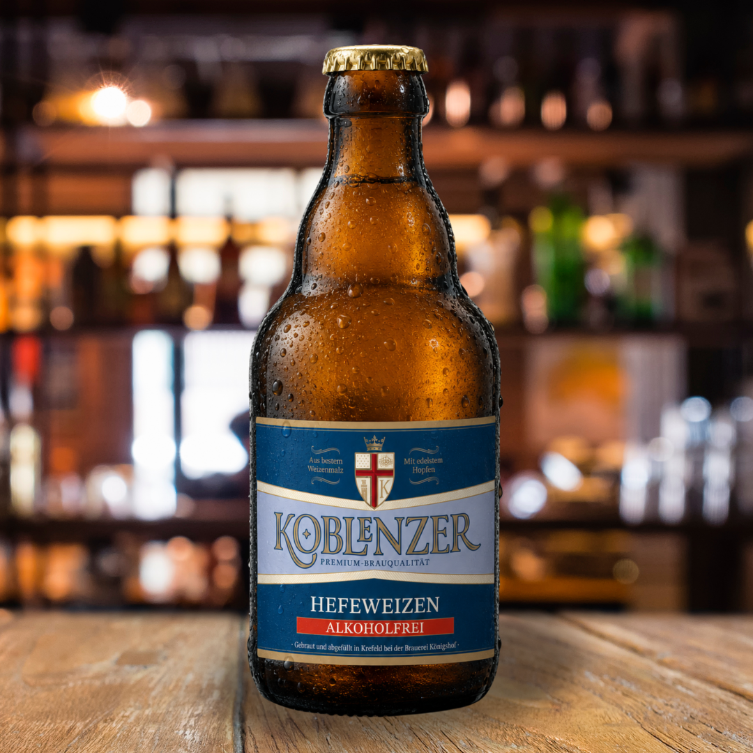 Flasche Koblenzer Hefeweizen alkoholfrei auf einem Holztisch vor unscharfem Barhintergrund.